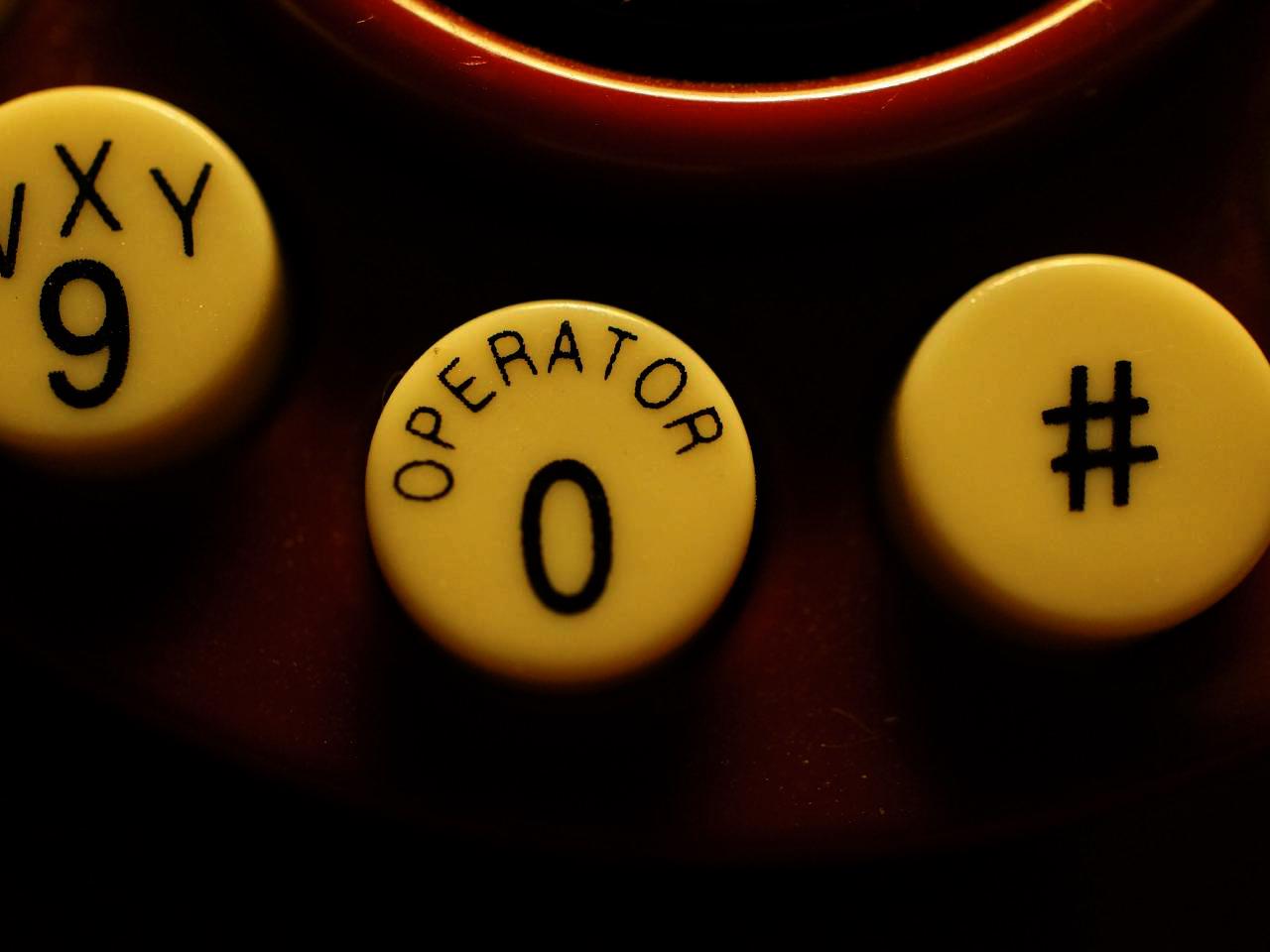 Close-up of vintage telephone keypad buttons, with a yellowed 0 OPER button in the center.