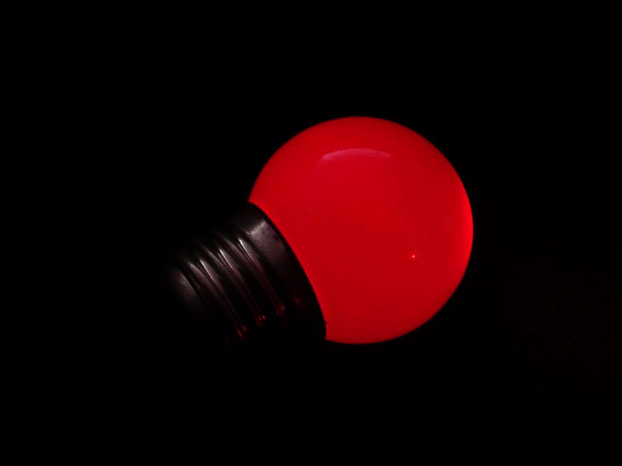 A red LED bulb is illuminated on a black background. The bulb is not connected to a socket.
