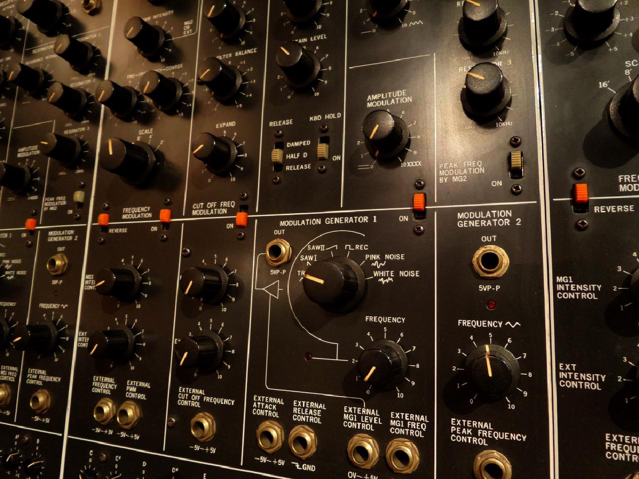 Close-up image of the control panel for a vintage analog synth, with rows of physical buttons, dials, and quarter-inch phono jacks.