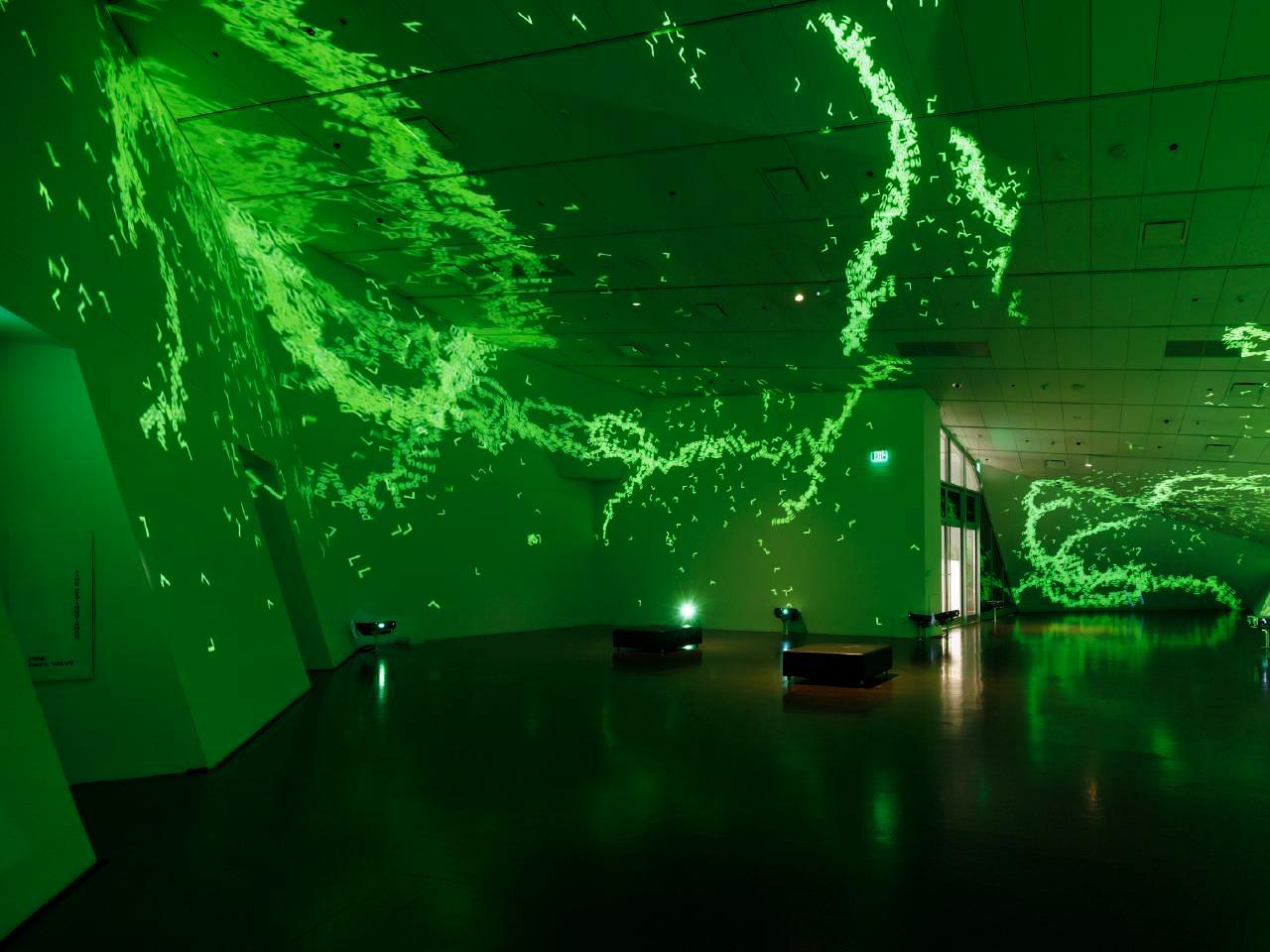 Image shows a single empty gallery with dramatically sloping walls. Streams of individual digital characters are projected onto the walls and ceilings