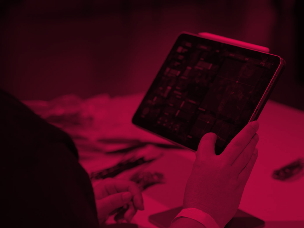 A person holds and operates a tablet computer with their right hand. The image is overlaid with a strong magenta filter.